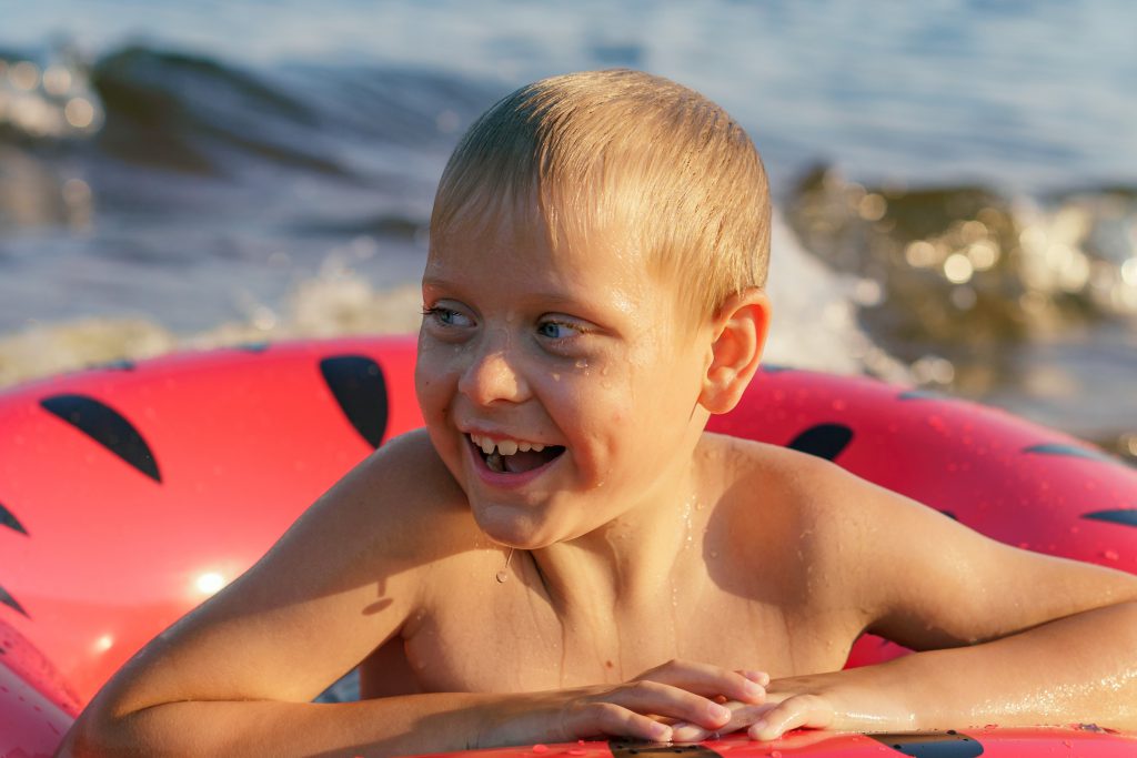 Happy cute caucasian boy swimming in watermelon inflatable ring. Vacation on sea side. High quality photo