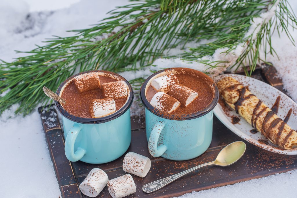 Two hot cocoa drink on a bed of snow and white background, close up. Concept of christmas winter morning