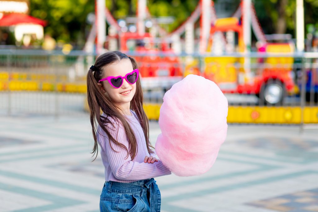 a child girl in an amusement park in the summer eats cotton candy near the carousels in sunglasses, the concept of summer holidays and school holidays