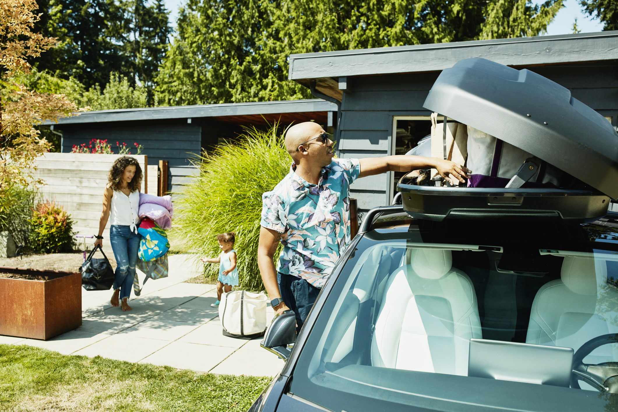 Family loading luggage into car top box before road trip